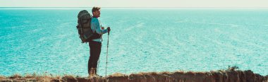 Sırt çantalı gezgin denizin üstündeki dağın tepesinde duruyor.