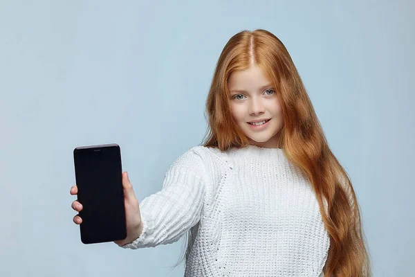 Uzun kızıl saçlı genç kız akıllı telefon gösteriyor.