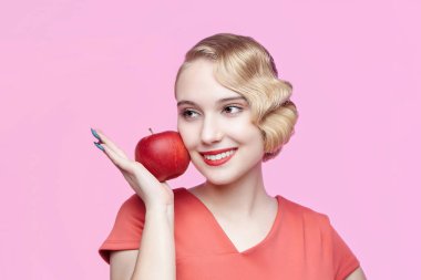 Geçmişe dönük saç stili olan çekici genç sarışın yüzünde kırmızı bir elma tutuyor.