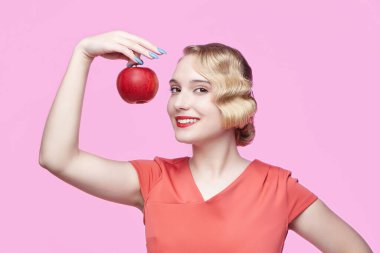 Eski saç stili olan çekici genç bir sarışın elinde kırmızı bir elma tutuyor.