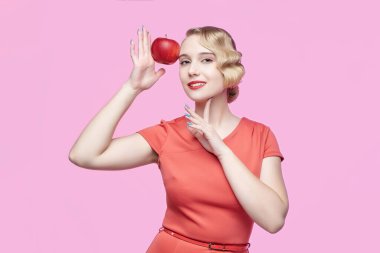 Geçmişe dönük saç stili olan çekici genç sarışın yüzünde kırmızı bir elma tutuyor.