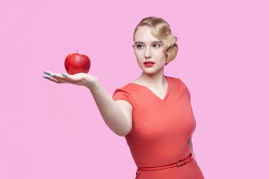 Eski saç stili olan çekici genç bir sarışın elinde kırmızı bir elma tutuyor.