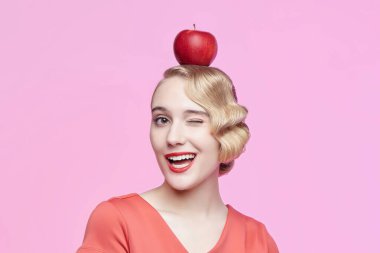 Saçları eski moda ve kafasında kırmızı bir elma olan çekici bir sarışın.