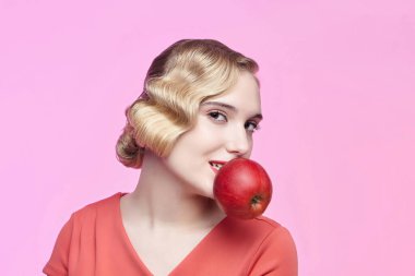 Eski saç stili olan çekici genç bir sarışın dişlerinde kırmızı bir elma tutuyor.
