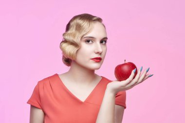 Eski saç stili olan çekici genç bir sarışın elinde kırmızı bir elma tutuyor.