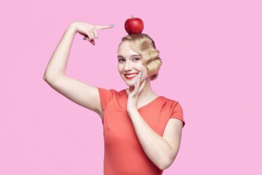 Retro saç stili çekici genç sarışın parmağını kırmızı bir elmaya doğrultuyor.