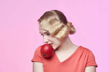 Eski saç stili olan çekici genç bir sarışın dişlerinde kırmızı bir elma tutuyor.
