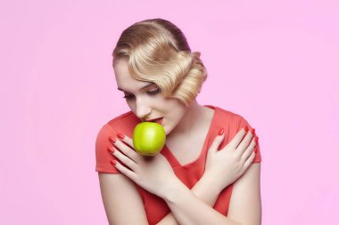 Eski saç stili olan çekici genç bir sarışın dişlerinde yeşil bir elma tutuyor.