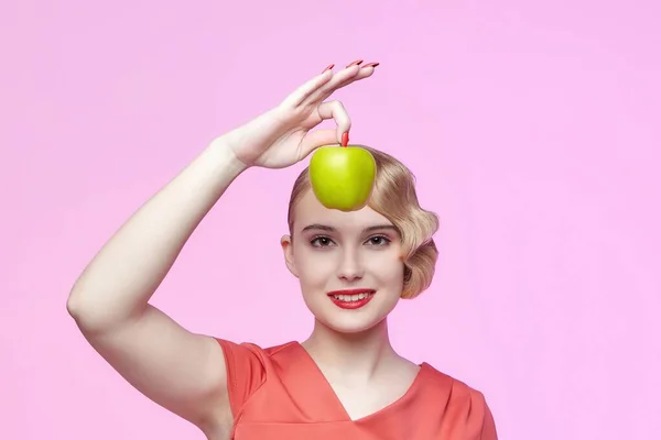 Eski moda saç stili olan çekici genç bir sarışın. Yüzünün yanında yeşil bir elma tutuyor.