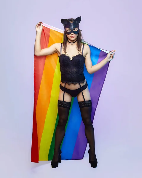 a woman in a cat mask holds a rainbow flag.