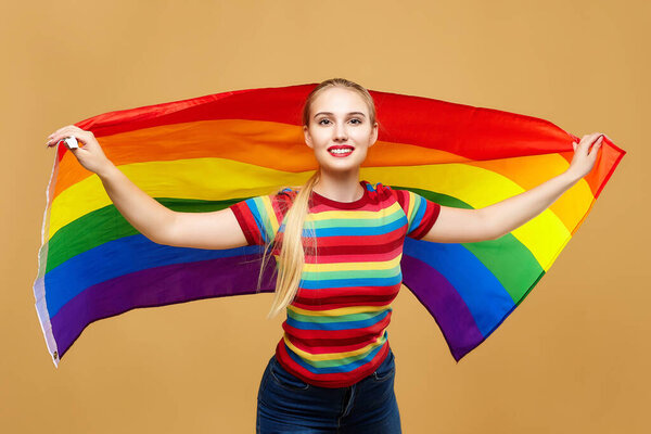 привлекательная блондинка, позирующая с радужным ЛГБТ-флагом. фотосессия в студии на желтом фоне.