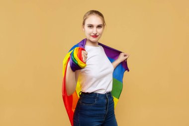 Gökkuşağı LGBT bayrağıyla poz veren çekici bir sarışın. Stüdyoda sarı arka planda fotoğraf çekimi..