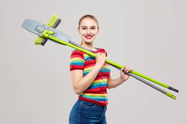 Çekici sarışının elinde paspas ve fırça var. Fotoğraf evi temizliği ve ev ödevi konsepti.