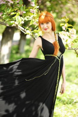 Genç ve güzel bir kadın, siyah, uzun elbiseli, bahar bahçesinde çiçek açan sakura 'nın arka planında..