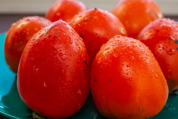 熟したジューシーなオレンジの柿を青緑色の皿に盛り — ストック写真