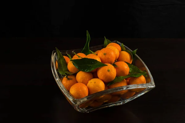 Glass vase with tangerines. Decor for the New Year and Christmas. stands in a glass vase on a black background, top view —  Fotos de Stock