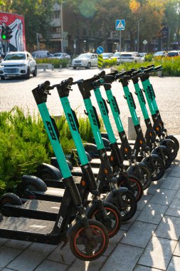 Taşkent, Özbekistan, Ekim 2025. Elektrikli scooterlar güneş ışığında şehir sokağına park edilmiş. Arabaları ve şehir arka planı var. Paylaşılan eko taşıma kavramı