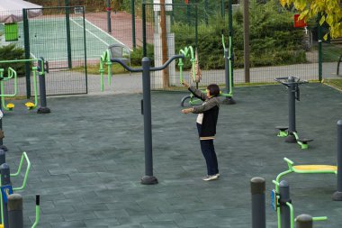 Taşkent, Özbekistan, 9 Ekim 2025: İnsanlar şehir parkında açık spor aletleri kullanıyorlar. Spor aletleri ve yeşil çevresi olan halka açık spor alanı, sağlıklı yaşam tarzını ve açık hava sporlarını destekliyor.