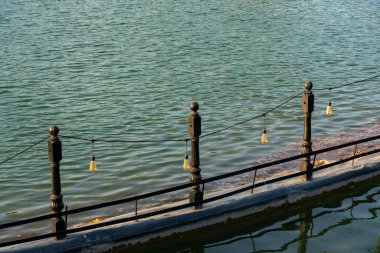 Sakin yeşil suyun üzerinde asılmış eski soğanları olan bir rıhtım korkuluğunun yakın görüntüsü. Sıcak akşam ışığında en az şehir detayı