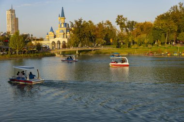 Taşkent, Özbekistan, 18 Ekim 2025: Pedal botlu manzara gölü ve arka planda şato benzeri bir bina, eğlence, doğa ve kentsel cazibeyi harmanlayan