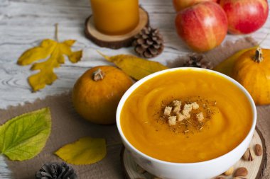 Kabaklarla, elmalarla, kozalaklarla ve kırsal ahşap masadaki sonbahar yapraklarıyla çevrili kremalı balkabağı çorbası. Sonbahar ya da Şükran Günü temaları için mükemmel