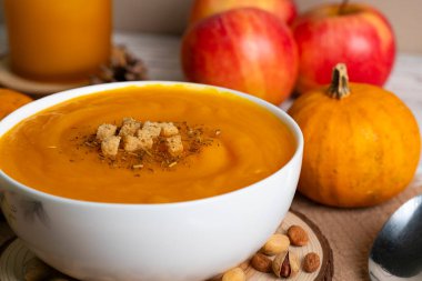 Kabaklarla, elmalarla, kozalaklarla ve kırsal ahşap masadaki sonbahar yapraklarıyla çevrili kremalı balkabağı çorbası. Sonbahar ya da Şükran Günü temaları için mükemmel