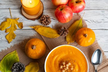 Sıcak sonbahar sahnesinde kremalı balkabağı çorbası, kızarmış ekmek, elma, balkabağı, kozalak ve mum ışığı. Sonbahar tarifleri, yemek blogları ve mevsimsel promosyonlar için mükemmel.