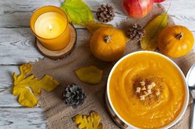 Sıcak sonbahar sahnesinde kremalı balkabağı çorbası, kızarmış ekmek, elma, balkabağı, kozalak ve mum ışığı. Sonbahar tarifleri, yemek blogları ve mevsimsel promosyonlar için mükemmel.