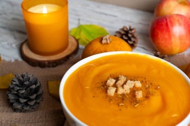 Sıcak sonbahar sahnesinde kremalı balkabağı çorbası, kızarmış ekmek, elma, balkabağı, kozalak ve mum ışığı. Sonbahar tarifleri, yemek blogları ve mevsimsel promosyonlar için mükemmel.