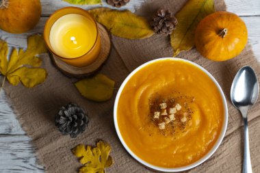 Sıcak sonbahar sahnesinde kremalı balkabağı çorbası, kızarmış ekmek, elma, balkabağı, kozalak ve mum ışığı. Sonbahar tarifleri, yemek blogları ve mevsimsel promosyonlar için mükemmel.