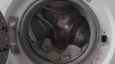 Modern bir çamaşır makinesinin variline beyaz giysiler yükleyen bir kadının yakın çekimi. Çamaşır yıkama kavramı