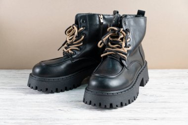 Açık ahşap arka planda bej bağcıklı şık siyah deri çizmeler. Sonbahar ve kış sezonu için moda ayakkabıları