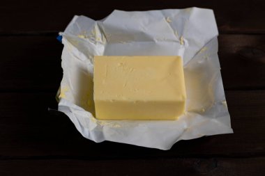 Koyu ahşap arka planda beyaz ambalaj kağıdında taze tereyağı. Pişirme ve pişirme için doğal süt ürünleri