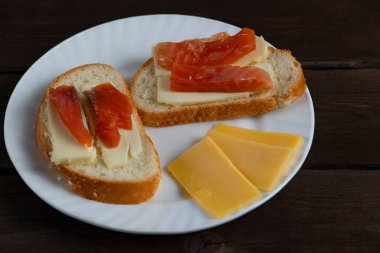 Tereyağlı ev yapımı sandviçler ve beyaz tabakta kırmızı balık dilimleri ve koyu ahşap arka planda peynir. Kahvaltı ya da yemek blogu temaları için mükemmel