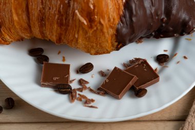 Çikolataya kısmen batırılmış taze kruvasan kahve çekirdekleri ve çikolata parçalarıyla beyaz bir tabakta servis ediliyor. Lezzetli bir kahvaltı veya yakın plan tatlı yemeği.