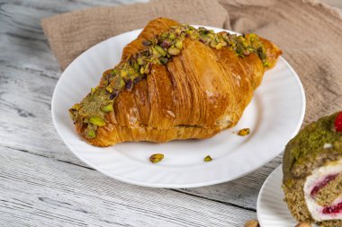 Çeşit çeşit şam fıstığı tatlıları ve bir fincan kahveyi kırsal ahşap bir masada. Kruvasan, kek ve fındık rahat bir kahvaltı ya da kafe tarzı yemek sahnesi oluşturur.