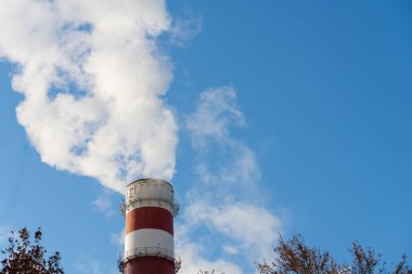 Endüstriyel baca açık mavi gökyüzüne beyaz duman salıyor. Hava kirliliği, endüstriyel emisyonlar, çevresel etki, enerji üretimi ve iklim değişikliği kavramı