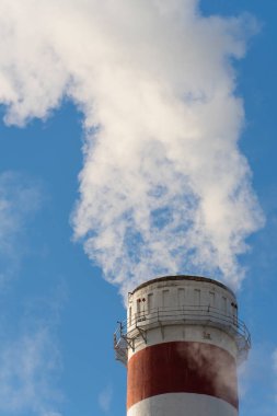 Endüstriyel baca açık mavi gökyüzüne beyaz duman salıyor. Hava kirliliği, endüstriyel emisyonlar, çevresel etki, enerji üretimi ve iklim değişikliği kavramı