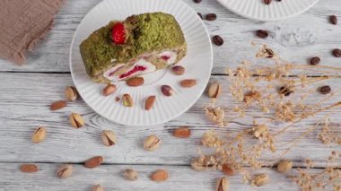 Beyaz tabakta kremalı ve meyveli fıstıklı bir fıstığın sinematik yakın çekimi. Hareket eden kamera fıstık, kahve çekirdekleri, kakao ve kurutulmuş çiçekleri, rahat bir kafe tatlı havasını ortaya çıkarıyor.