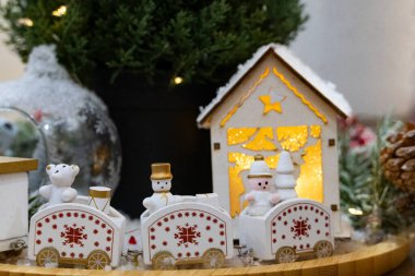 Beyaz ve altın minyatür bir tren, kardan adam ve ayı heykelcikleri, çam dalları ve sıcak Noel ışıklarının yer aldığı samimi bir tatil sahnesi.