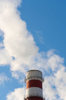 Açık bir kış gününde yapraksız ağaçlarla çerçevelenmiş, duman çıkaran elektrik santrali bacaları. Enerji üretimi ve çevresel etkiyi vurgulayan editoryal görüntü