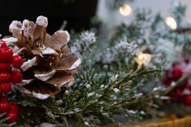 Kırmızı böğürtlenlerle, kozalaklarla ve yapay karla kaplı yeşil dallarla süslü Noel süslemeleri. Sıcak ışıklı sıcak tatil atmosferi mevsimlik arka planlar ve kış tasarımı için mükemmel.