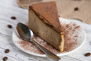 Kakao tozu ve kaşıkla beyaz tabakta bir dilim peynirli keki yakından çek. Asgari gıda tasarımı, kremsi doku, rahat tatlı konsepti, kafe menüleri ve yemek tasarımı için mükemmel.