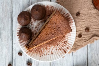 Sıcak tatlı sahnesinde bir dilim kahve aromalı cheesecake ve kırsal bir arka planda kakao tozlu trüf var.