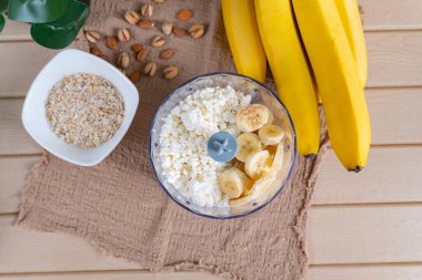 Köhne bir mutfak masasında süzme peynir ve dilimlenmiş muz. Doğal malzemelerle sağlıklı kahvaltı hazırlama, temiz yemek, ev yapımı gıda konsepti.