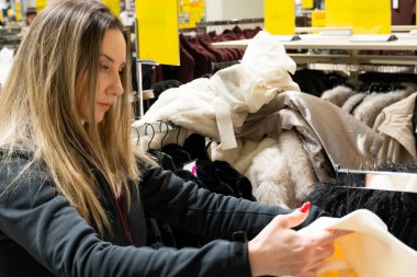Modern bir perakende mağazasının rafında bayan müşterilerin kıyafetlerini karıştırıyor. Moda dükkanında alışveriş yaparken giyinmeyi seçen kadın.