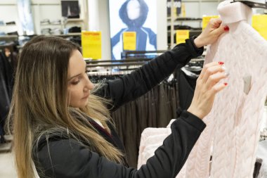 Modern bir perakende mağazasının rafında bayan müşterilerin kıyafetlerini karıştırıyor. Moda dükkanında alışveriş yaparken giyinmeyi seçen kadın.