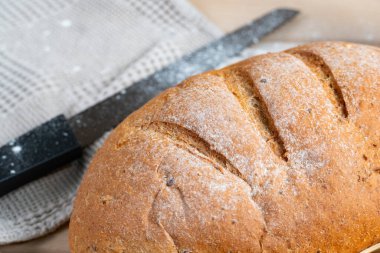 Un tozlu ekmek ile altın-kahverengi zanaatkar ekmek ahşap yüzey, bıçak, bez ve kırsal bir mutfak için buğday sapları eşliğinde dinlenir