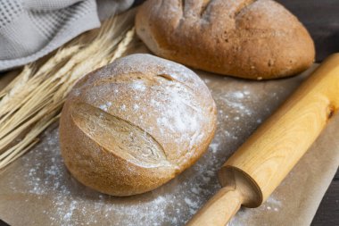 İki zanaatkar ekmek, parşömen üzerinde buğday sapları ve merdaneyle dinlenerek doğal malzemelerle ev yapımı sıcak bir pişirme sahnesi yaratıyor.