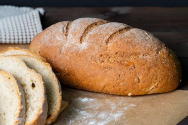 Taze pişmiş rustik ekmek somunu ahşap yüzeyde kısmen dilimlenmiş, buğday sapları ve bez ile eşleştirilmiş, sağlıklı bir çiftlikten sofraya hissi için.